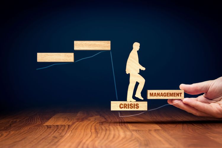 Person stepping from a block labeled "CRISIS" to a block labeled "MANAGEMENT," with a hand supporting the "MANAGEMENT" block.