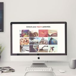Portfolio Website Design at its Finest 11 A desktop computer showing a website with a grid of images and the text "Unlock your digital potential." There is a poster on the wall that says "Build it your way."