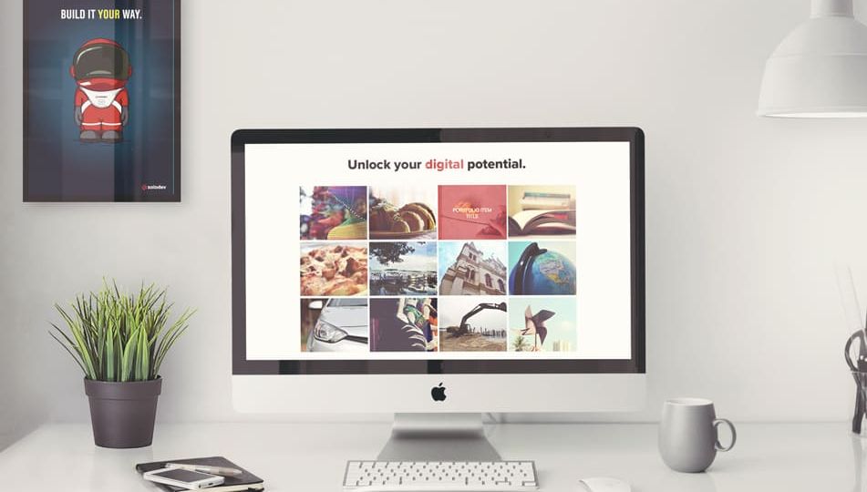 A desktop computer showing a website with a grid of images and the text "Unlock your digital potential." There is a poster on the wall that says "Build it your way."